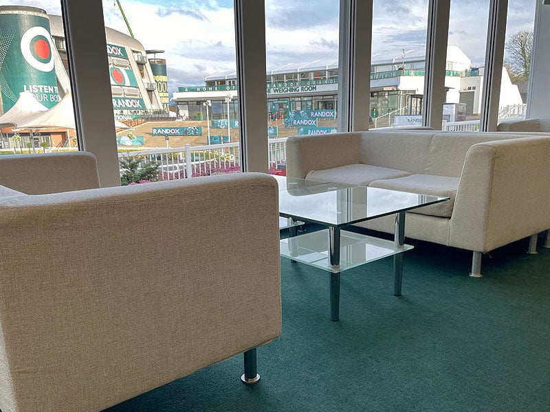 Lounge area with cream sofas and a glass coffee table beside large windows overlooking buildings displaying Randox signage.