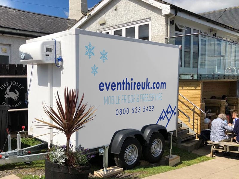 White refrigerated trailer parked beside a building, branded “eventhireuk.com” with mobile fridge and freezer hire details and the phone number 0800 533 5429.